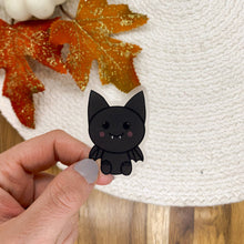 Load image into Gallery viewer, Hand holding cute black bat vinyl sticker with autumn leaves and white sweater background