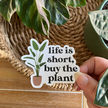 Load image into Gallery viewer, Hand holding white sticker with plant illustration reading 'life is short, buy the plant'