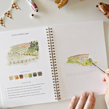 Load image into Gallery viewer, Open spiral-bound watercolor workbook showing farm landscape painting tutorial with color palette and instructions