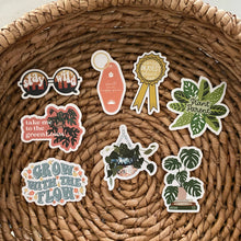 Load image into Gallery viewer, Collection of plant-themed vinyl stickers with sayings like 'Plant Parent' and 'Grow with the Flow' on woven basket