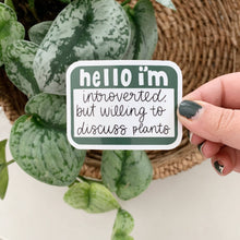 Load image into Gallery viewer, Hand holding green sticker reading 'hello i'm introverted but willing to discuss plants' near houseplant