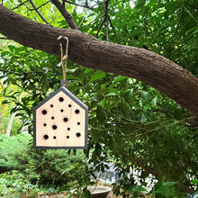 Load image into Gallery viewer, Wooden bee house with multiple holes hanging from tree branch in garden
