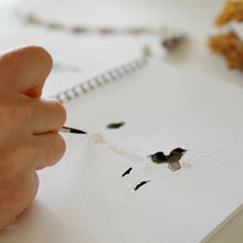 Load image into Gallery viewer, Hand holding watercolor brush painting farm animals in spiral-bound art workbook