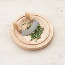 Load image into Gallery viewer, Circular rubberwood cutting board with stainless steel mezzaluna knife and fresh chopped herbs