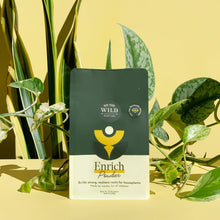 Load image into Gallery viewer, We The Wild Enrich Powder plant fertilizer package surrounded by green houseplants