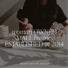 Load image into Gallery viewer, Woman holding pen at desk with coffee mug and candle, woman-owned business text overlay
