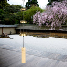 Load image into Gallery viewer, Brass wind chimes with three graduated bells and wooden clapper hanging in zen garden