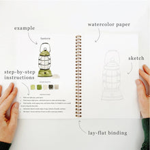 Load image into Gallery viewer, Spiral-bound camping watercolor workbook open showing lantern tutorial with sketch and example pages