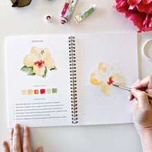 Load image into Gallery viewer, Hands painting yellow hibiscus flower in watercolor workbook with color palette and instructions