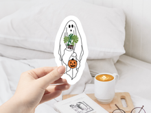 Load image into Gallery viewer, Hand holding white ghost sticker with plant head and pumpkin, coffee cup nearby