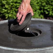 Load image into Gallery viewer, Hand installing black ribbed pump component into circular stone fountain basin outdoors