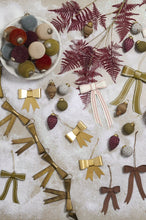 Load image into Gallery viewer, Gold, olive, and brown bow-shaped Christmas ornaments displayed on faux snow with holiday decorations