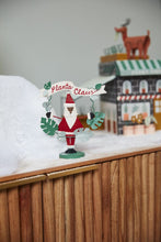 Load image into Gallery viewer, Planta Claus wooden Santa figurine with monstera leaf wreath and banner on snowy display