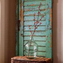 Load image into Gallery viewer, Red ilex berry stems displayed in a clear glass vase against a rustic turquoise shutter backdrop