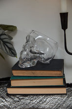 Load image into Gallery viewer, Clear glass skull-shaped decorative pot displayed on stacked vintage books with candle holder